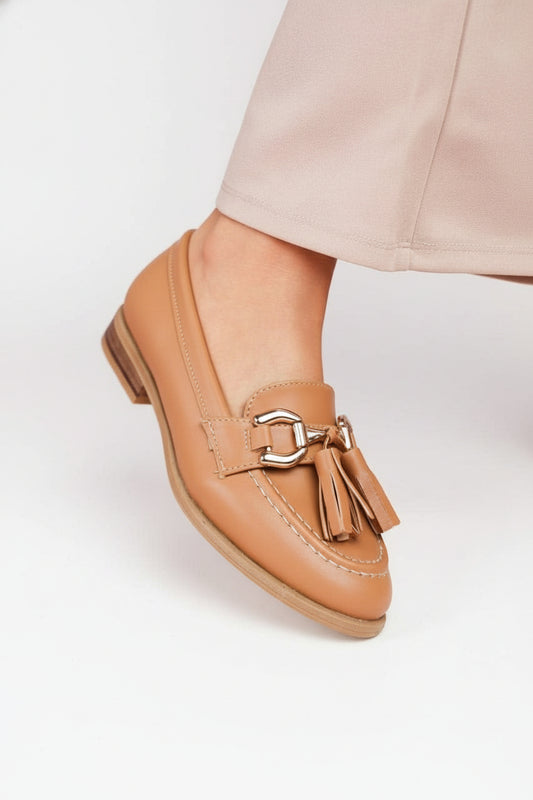 Tan loafers with a tassel detail worn by a person on a light background