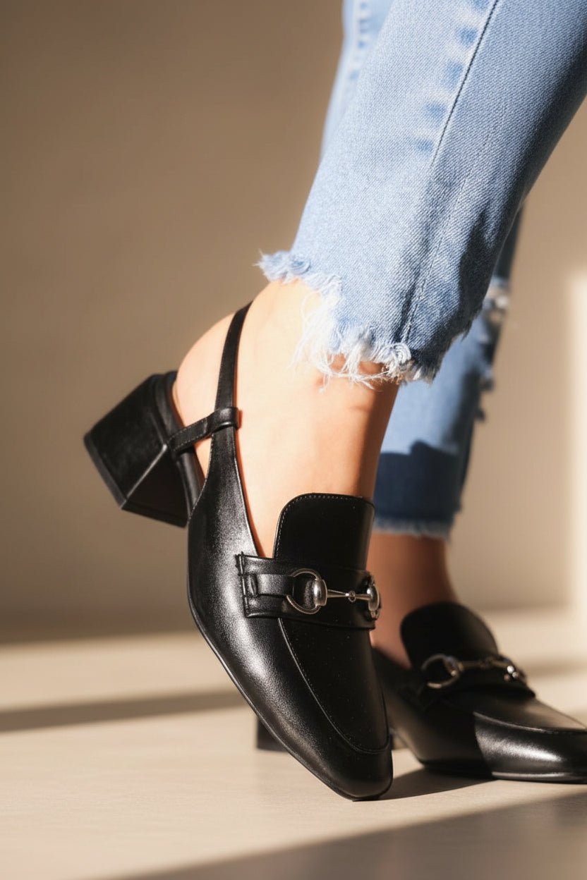 Black leather shoe with a strap worn by a person, on a neutral background